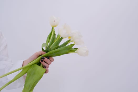 Bouquet of white tulips on woman's hand. Gift concept. Gift idea for lover, mother, sister, birthday, engagement day, anniversary. Closeup. White background. Copy space.