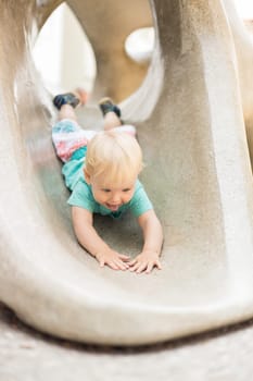 Child playing on outdoor playground. Toddler plays on school or kindergarten yard. Active kid on stone sculpured slide. Healthy summer activity for children. Little boy climbing outdoors