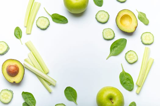 Bottle of green smoothie surrounded by green fruit and vegetables: apples, avocado, spinach, celery sticks, cucumber on white simple background top view. Diet, healthy nutrition, detox concept