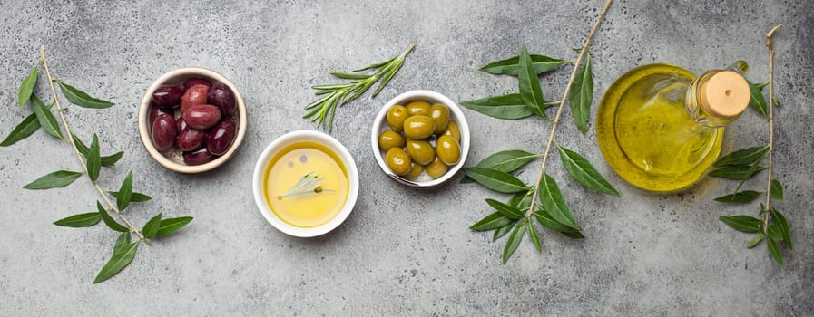 Composition with green and brown olives, extra virgin olive oil in glass bottle, olive tree branches on gray concrete stone rustic background overhead, Mediterranean concept