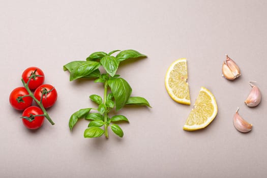 Composition with healthy food ingredients: branch of fresh cherry tomatoes, basil branch, garlic cloves, lemon wedges on minimalistic gray clean background, overhead shot
