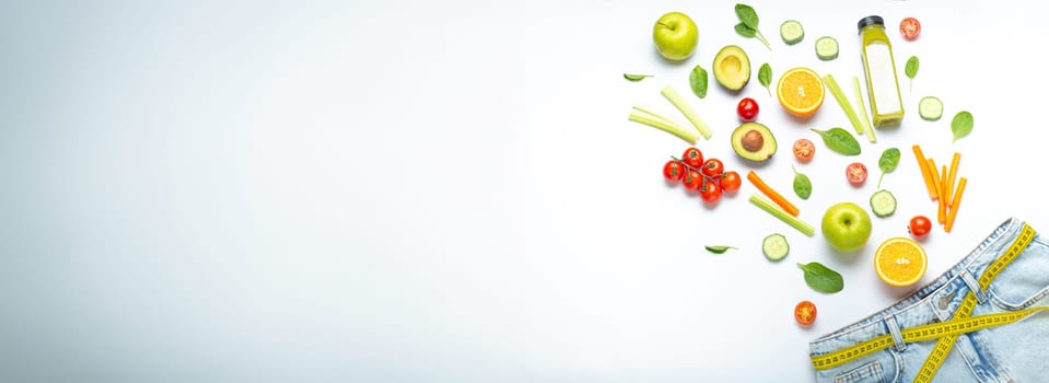 Fresh fruit, vegetables, smoothie falling into jeans and yellow measuring tape instead of belt on white background. Concept of weight loss, detox, diet, healthy clean nutrition, copy space