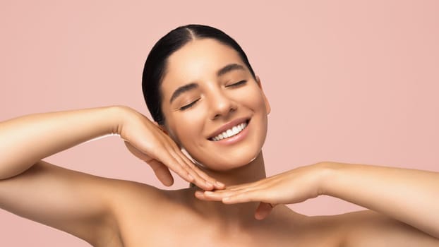 Beauty portrait of cheerful beautiful woman smiling with eyes closed tilted head and gentle hands next to face.