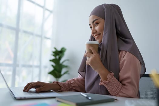 Portrait of a Muslim woman using laptop computer and drinking coffee