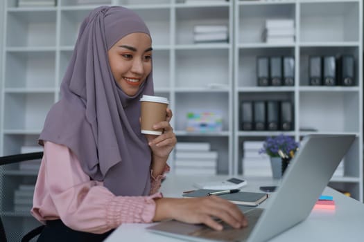 Portrait of a Muslim woman using laptop computer and drinking coffee