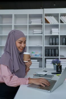 Portrait of a Muslim woman using laptop computer and drinking coffee