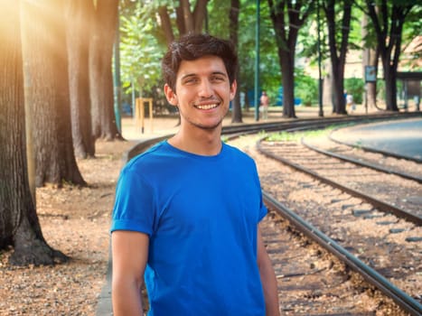 Three quarters shot of one handsome young man in urban setting wearing blue polo shirt, smiling to the camera