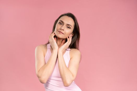 Touching her chin beautiful young woman with no makeup, skin care concept, attractive brunette girl on pink background. Human emotions, facial expression concept. Beauty concept.