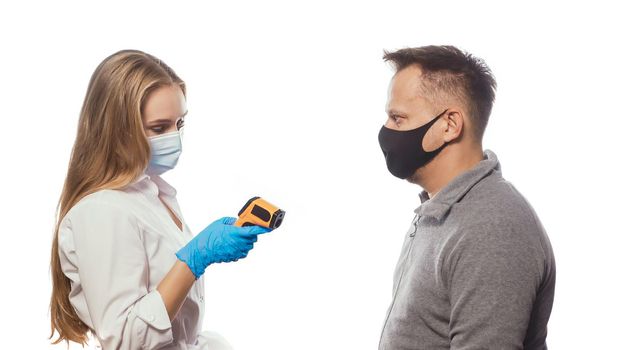 Looking at non-contact thermometer nurse testing employee's or patients body temperature wearing a medical face mask. Sad man wearing reusable face mask isolated on white background.