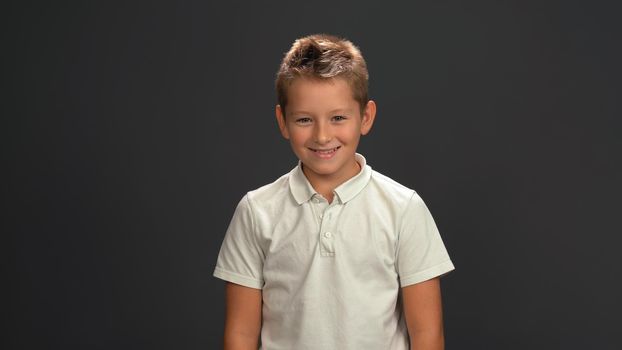 Cool happy smiling blond hair little boy in white shirt looking at camera Isolated on black background.