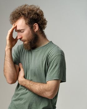 Has a headache or shame for an opponent young man touching his forehead. Handsome young man with curly hair in olive t-shirt isolated on white background.