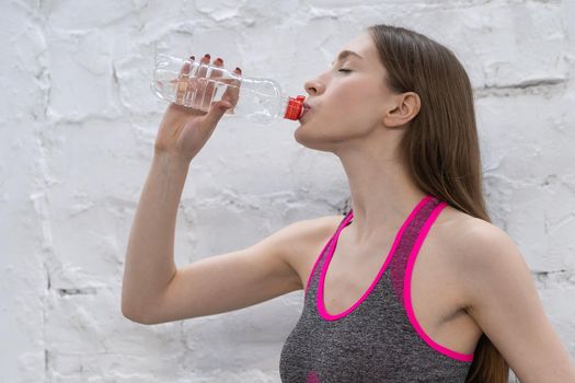Young athlete woman takes a break drinking water from plastic bottle. Young woman drinking water after working out in the gym, health and sport concept.
