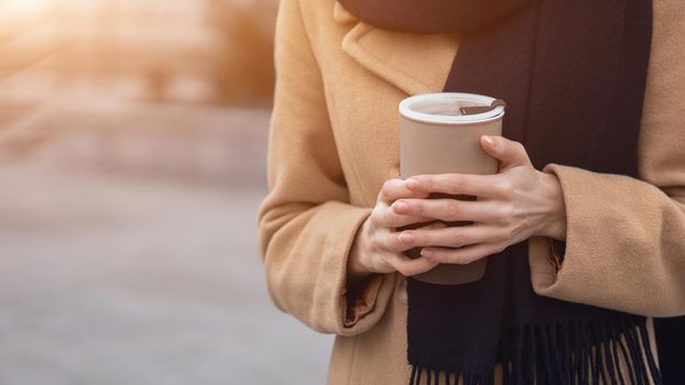 Close up on woman's hands holding a cup of coffee wearing beige coat on the street female fashion. Portrait of stylish young woman wearing autumn coat and red beret outdoors. Autumn accessories.