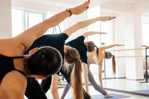 Group of attractive sport girls in sportswear working out in fitness hall. Young fit women doing yoga pose exercise on mats in gym. Concept of sport.