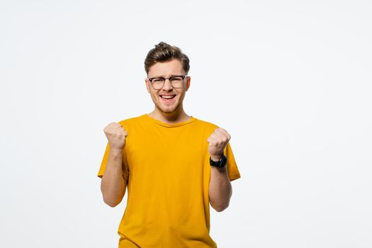 Casual man winning and celebrating handsome young man with hands lifted up. Young casual man portrait isolated on white background. Human emotions, facial expression concept.