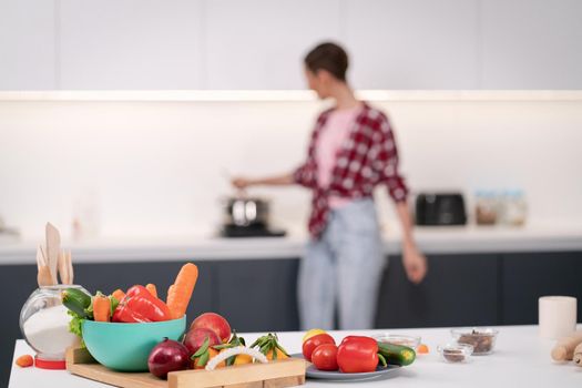 Selective focus on food with blurred woman on back. Cooking at new home for loving family. Preparing ingredients on table young woman cooking a lunch standing in the kitchen. New home concept.