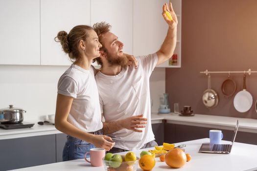 Hiding from a ray of lights shining from a window young couple making breakfast in kitchen at home. Girl hug husband smiling looking away. Beautiful young couple at kitchen.