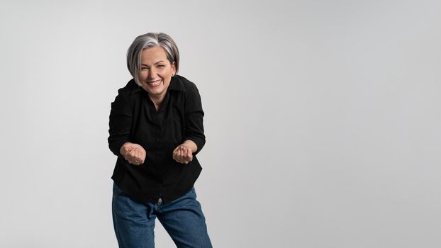 Happy to see her grand kids bowed and hands stretched forward grey haired mature woman wearing black shirt isolated on grey background. Human emotions, facial expression concept.