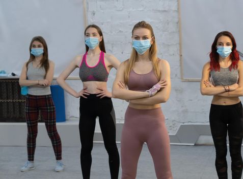 yoga during pandemic wearing medical face protective mask athletic girls in sports out fits standing in yoga class, standing one after another. Group of young sporty people practicing yoga lesson.