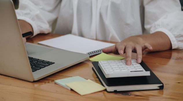 Close up accountant working on desk using calculator and laptop computer for calculate finance report in office