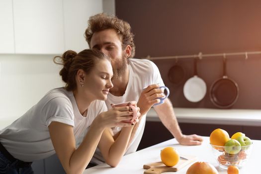 Morning coffee and gentle kissing feeding each other making fun at modern kitchen and smiling while cooking at home. Pretty girl feeds or nursing her boyfriend.