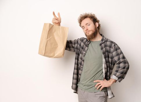 Holding paper bag young man in plaid shirt isolated on white background. Delivery concept. Paper bag for takeaway food. Courier with a bag on white background.