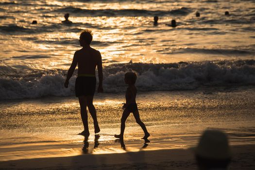 silhouettes of father and son on sunset beach sea