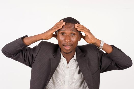 young man in suit standing on white background hands grabbing his head, looking at the camera with his mouth open.