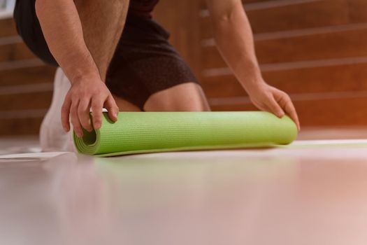 Wrapping UP after training a roll mat athletic man, preparing a place for sports. Determined guy doing physical training. Strong handsome young man, in a gym.