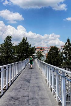 Lisbon, Portugal- 19 may, 2018: Woman in green dress crossing white bridge under blue sky with some clouds in Lisbon city