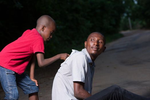 child in red tee shirt doing on the back of his father the one sitting on the floor.