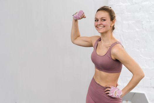 Strong woman showing biceps standing wearing pink outfit exercising at home. Sport and recreation concept. Pensive girl is enjoying with her training process working hard. sports concept.