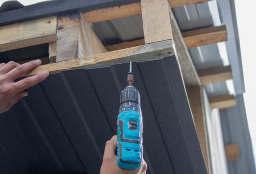 a man repairs the roof, tightens the self-tapping screw with a screwdriver. Selective focus