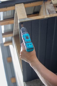a man repairs the roof, tightens the self-tapping screw with a screwdriver. Selective focus