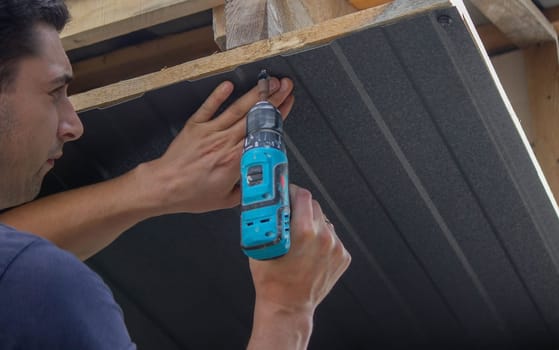 a man repairs the roof, tightens the self-tapping screw with a screwdriver. Selective focus