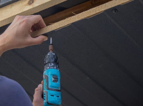 a man repairs the roof, tightens the self-tapping screw with a screwdriver. Selective focus