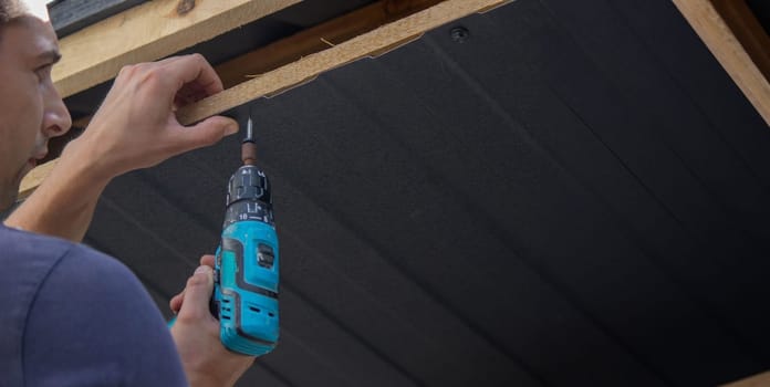 a man repairs the roof, tightens the self-tapping screw with a screwdriver. Selective focus