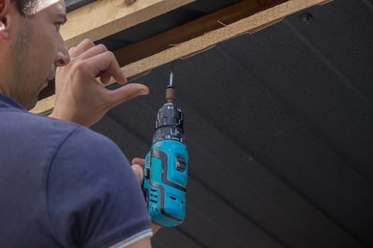 a man repairs the roof, tightens the self-tapping screw with a screwdriver. Selective focus