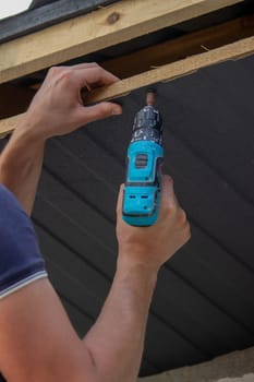 a man repairs the roof, tightens the self-tapping screw with a screwdriver. Selective focus