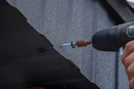 a man repairs the roof, tightens the self-tapping screw with a screwdriver. Selective focus