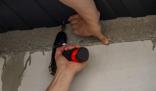 a man repairs the roof, tightens the self-tapping screw with a screwdriver. Selective focus