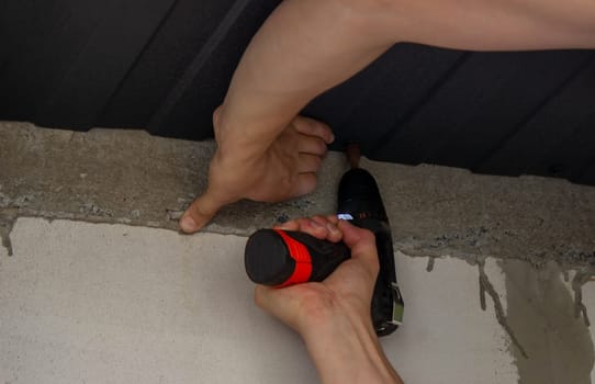 a man repairs the roof, tightens the self-tapping screw with a screwdriver. Selective focus