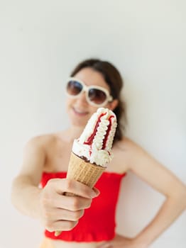 Happy cheerful girl in a red top and white sunglasses eats a colorful ice cream cone in her hands and smiles