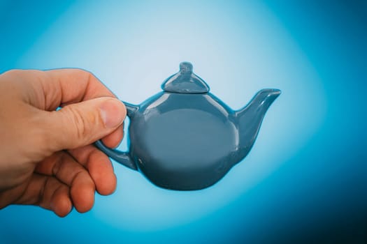 a small blue ceramic teapot for making tea in your hand on a blue background. Minimalist Ceramic Teapot