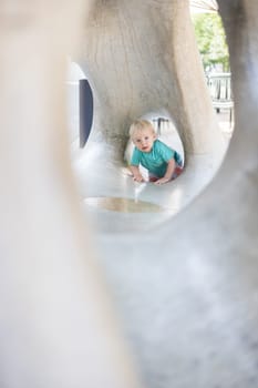 Child playing on outdoor playground. Toddler plays on school or kindergarten yard. Active kid on stone sculpured slide. Healthy summer activity for children. Little boy climbing outdoors