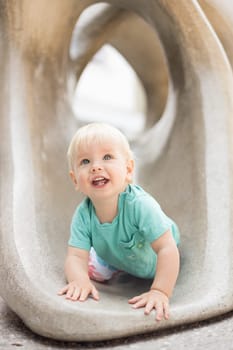 Child playing on outdoor playground. Toddler plays on school or kindergarten yard. Active kid on stone sculpured slide. Healthy summer activity for children. Little boy climbing outdoors