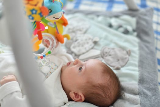 Baby boy playing with hanging toys on a developing mat