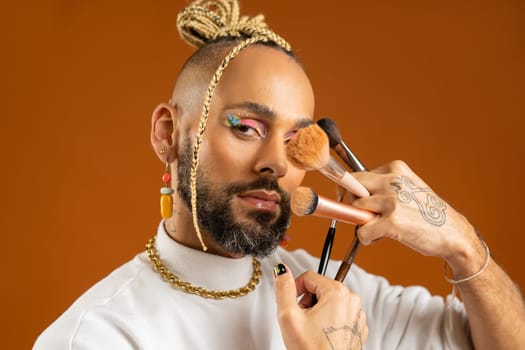 African american gay with bright make up holding makeup brush. Handsome guy wear bright make-up. Fashion lgbtq concept. Male makeup artist close up portrait