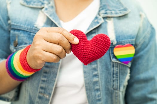 Asian lady wearing rainbow flag wristbands and hold red heart, symbol of LGBT pride month celebrate annual in June social of gay, lesbian, bisexual, transgender, human rights.