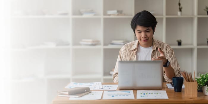 Young asian businessman connecting with his team online and using video call by laptop computer.